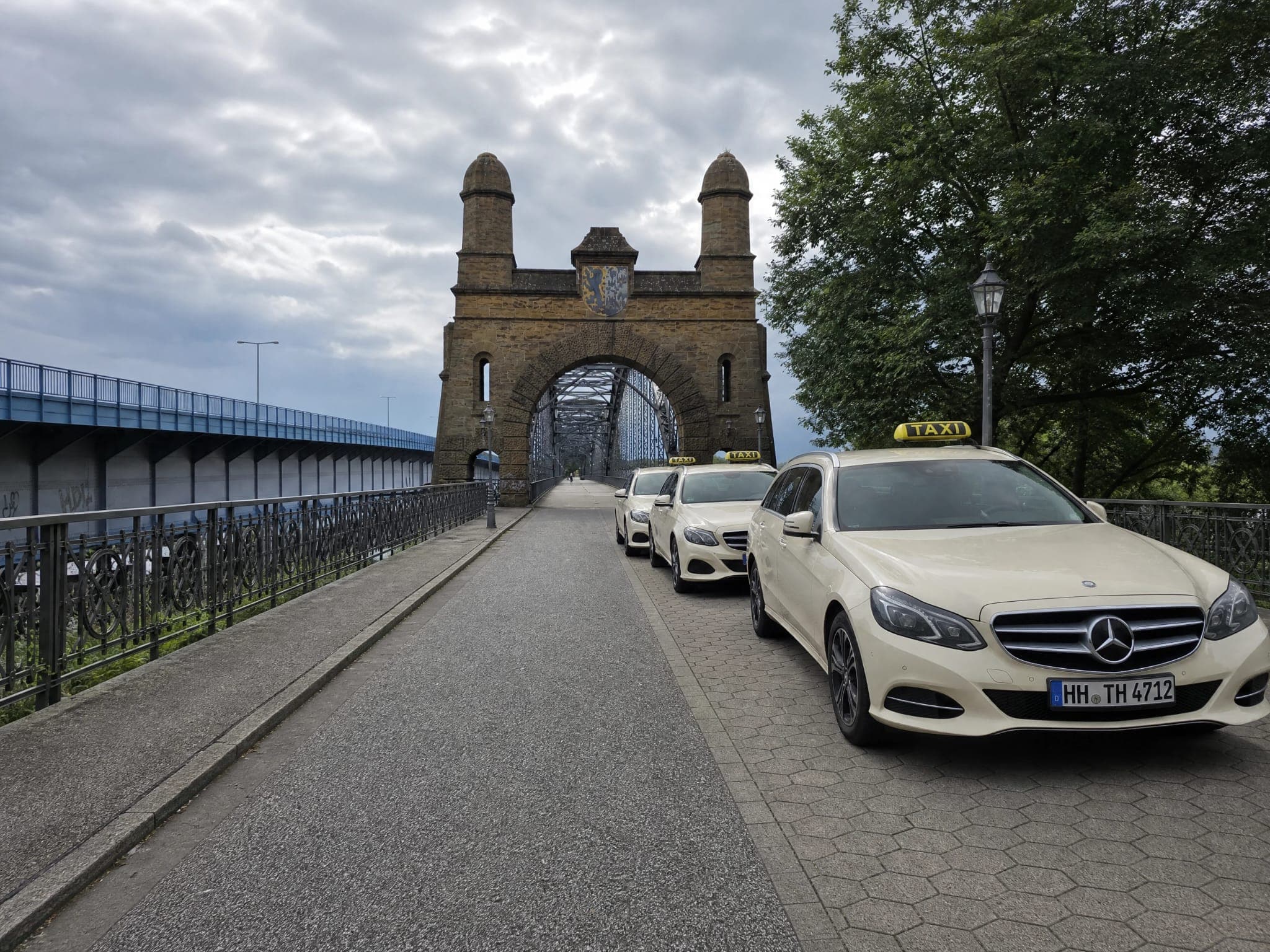 Drei helle Taxis stehen hintereinander auf der Alten Harburger Elbbrücke, dahinter das steinerne Brückentor mit zwei Türmen