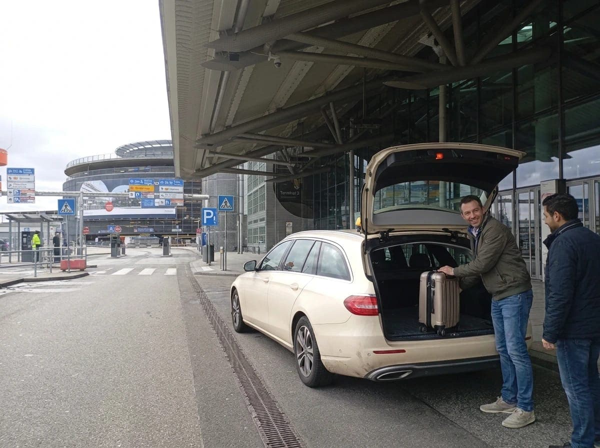 Ein Mann lädt vor dem Terminal des Hamburger Flughafens einen Koffer in den Kofferraum eines hellen Taxis, daneben ein zweiter Mann